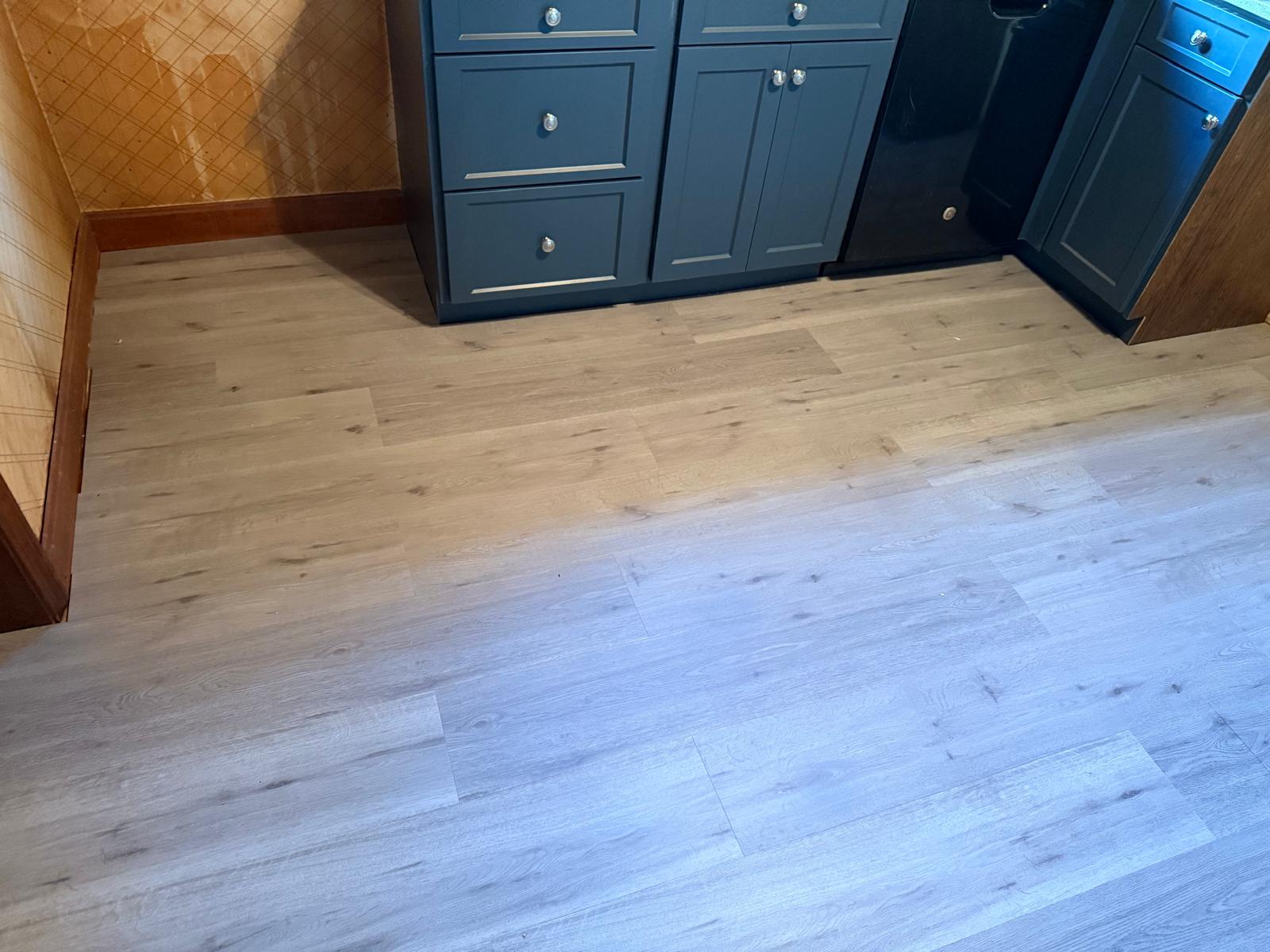 Finished light-tone plank flooring in a kitchen with blue cabinets